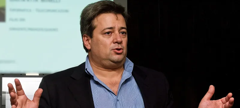 Marco Lungo parla a un evento, a mani aperte, davanti a uno schermo